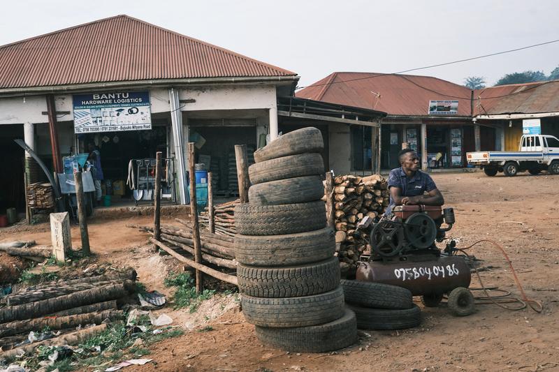Person sitting behind an air compressor in front of store fronts, Uganda