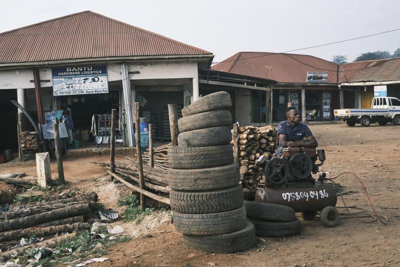 Person sitting behind an air compressor in front of store fronts, Uganda