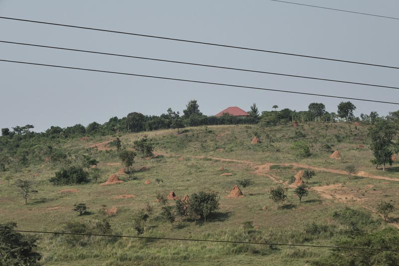 Hillside view with several large ant hills and a building that resembles the sun coming up over the horizon, Entebbe, Uganda