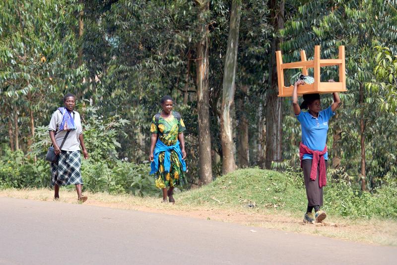 People walking along the street, one person is carrying a table on their head, Uganda