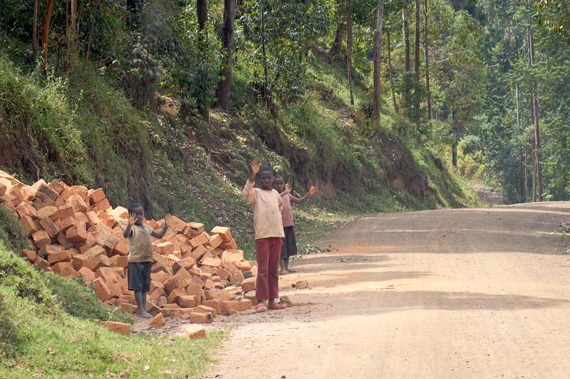 Three kids waving with their hands covered in brick dust, Uganda